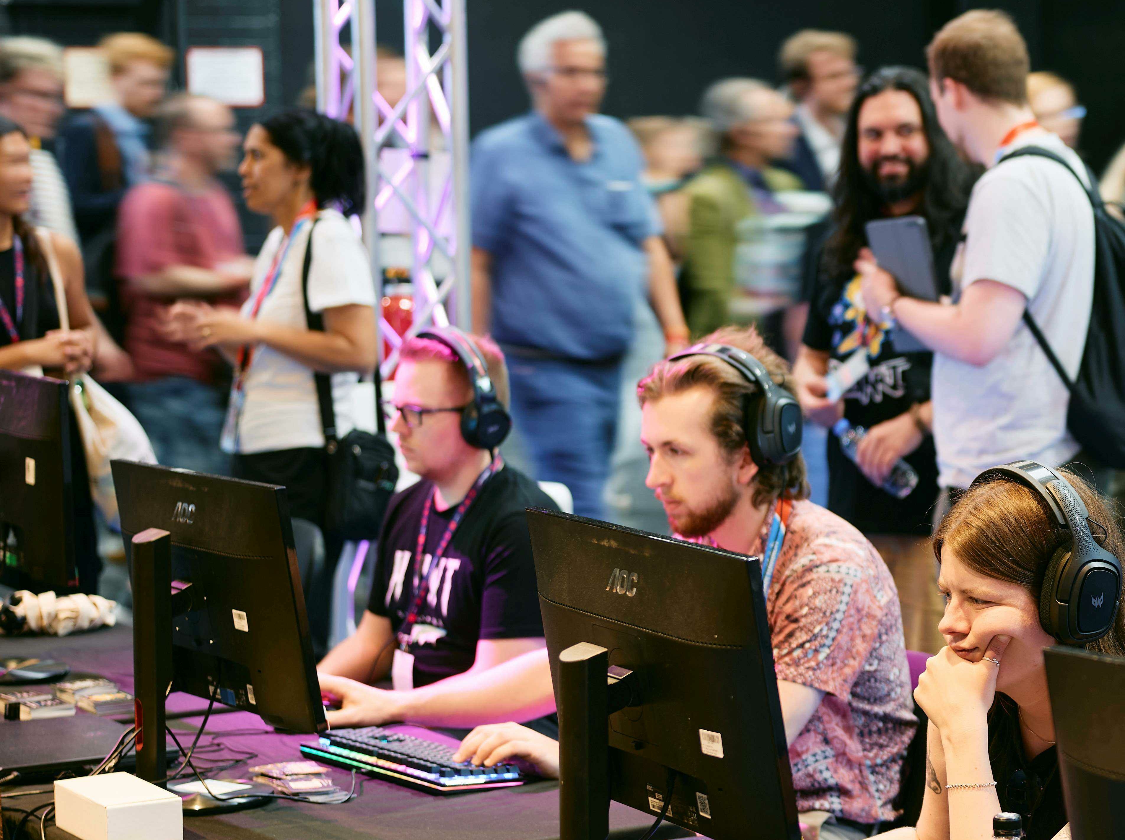 Leute sitzen an Monitoren bei Gamescom, Menschenmenge im Hintergrund
